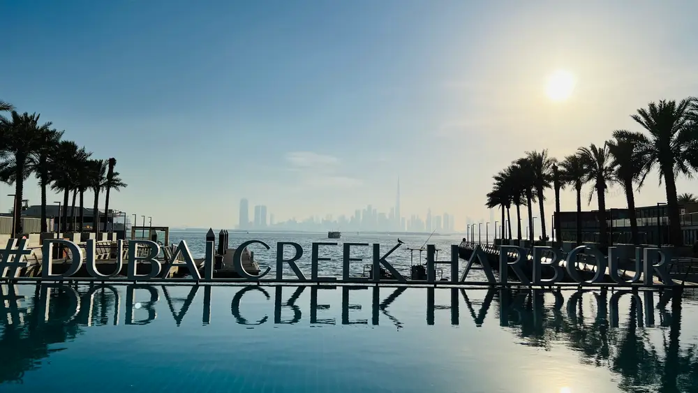 Infinity pool and palm trees beside the Dubai Creek Harbour sign at Creek Beach