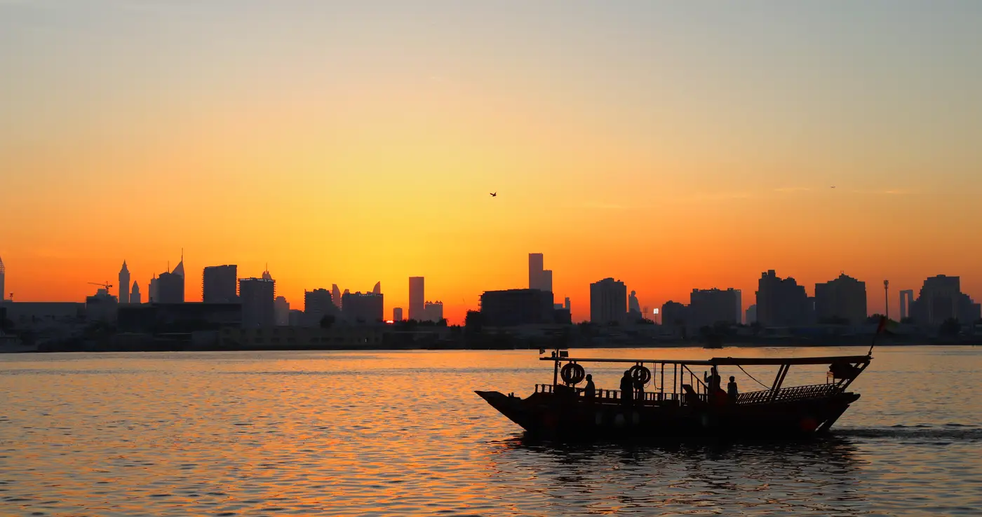 Traditional dhow crossing Dubai Creek at sunset with the city skyline behind